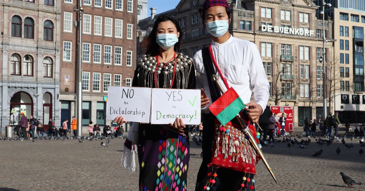 Two masked individuals in traditional attire protest for democracy in Amsterdam.